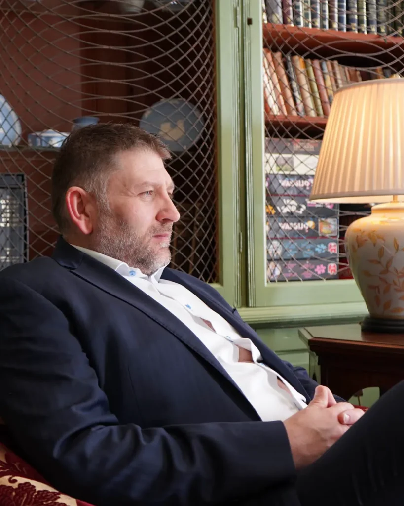 Richard Stone seated in a panelled library armchair wearing a navy blazer.
