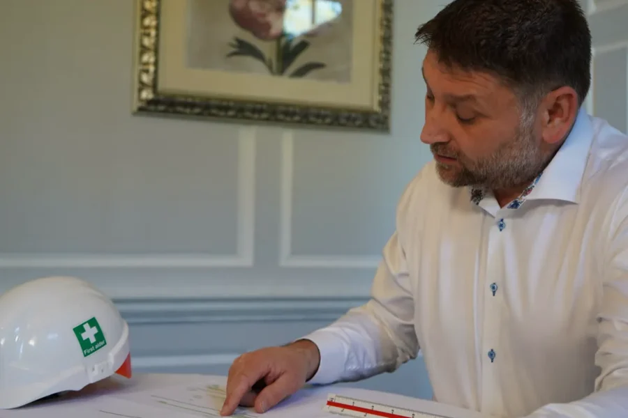 Richard Stone reviewing construction drawings at a desk, white hard hat in the foreground.